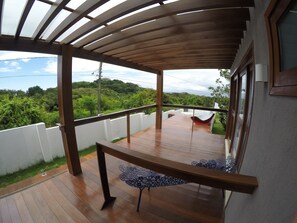 Una terraza de madera con barandilla de vidrio que da a un paisaje verde exuberante.