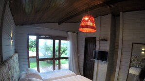 A bedroom with two beds, a TV, and a large window with a view of greenery. - Pousada Nascer do Sol (Fernando de Noronha)