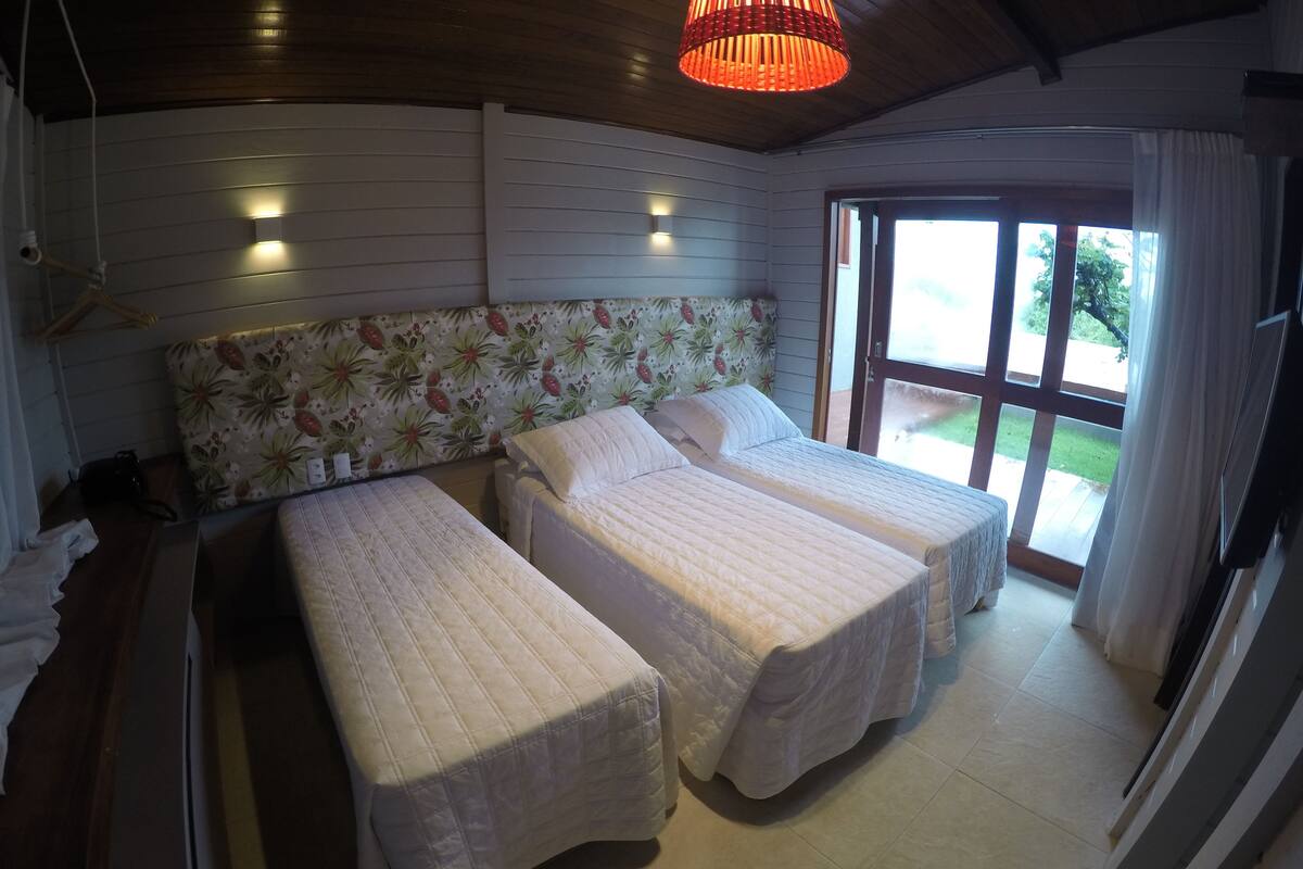A room with two beds, a wooden ceiling, and a large window with curtains.