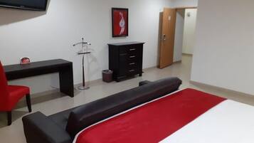 A bedroom with a bed, a desk, a chair, a wardrobe, and a television.