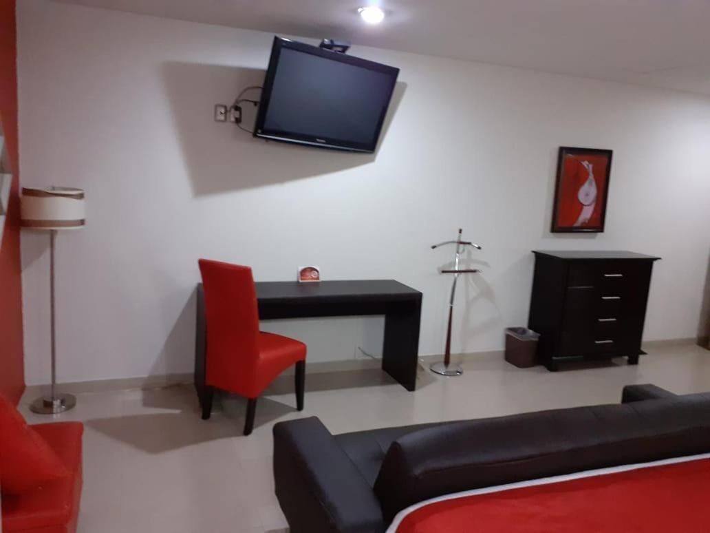 Una habitación con una televisión de pantalla plana montada en la pared, un escritorio con una silla, un armario negro y un sofá rojo.