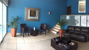 Un vestíbulo con pared azul, una recepción, un sofá de cuero negro y una mesa de centro con revistas.