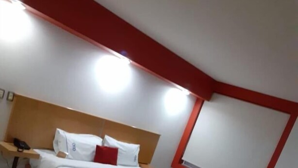 Una habitación de hotel moderna con cama, mesita de noche y una pared de acento roja.