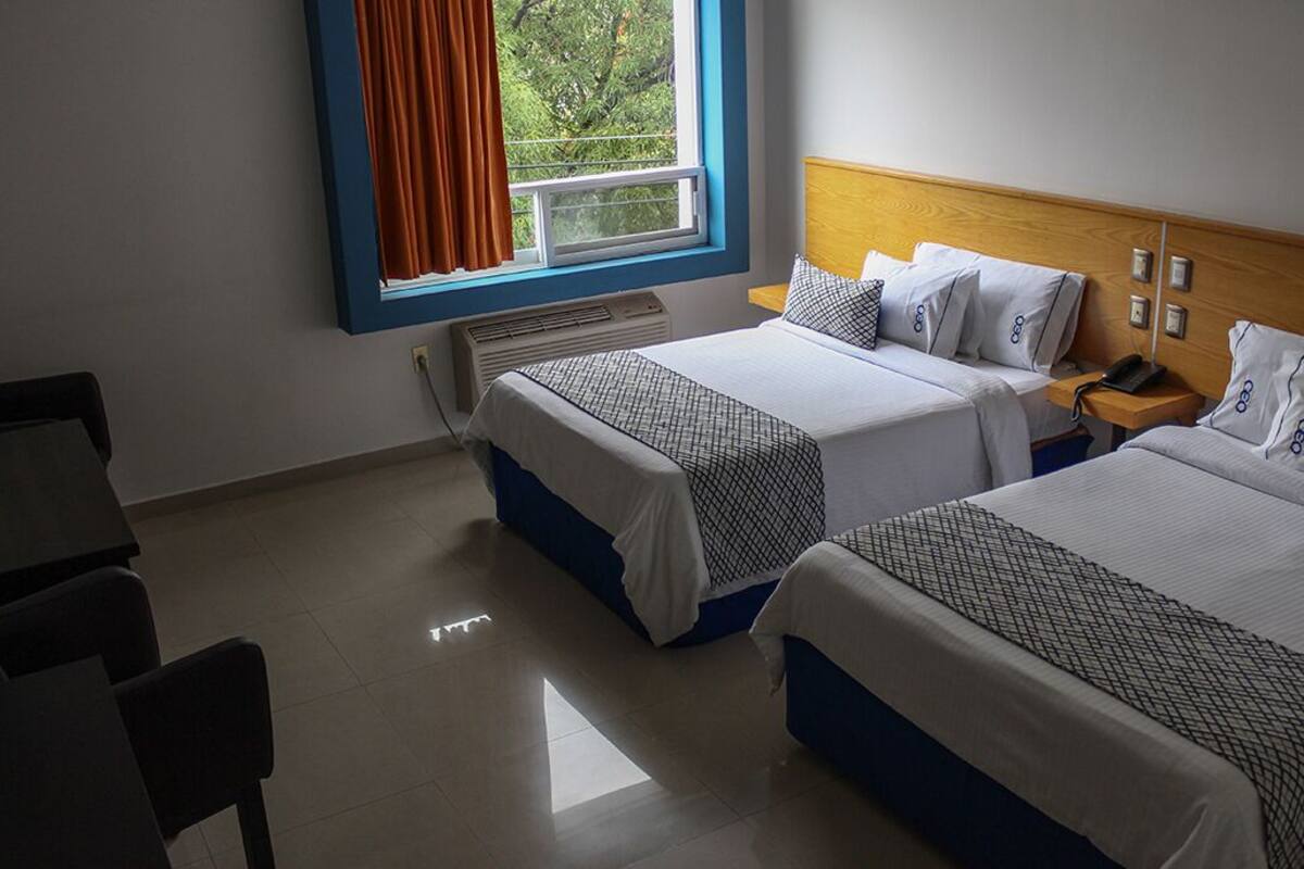 A hotel room with two beds, a desk, and a window with curtains.