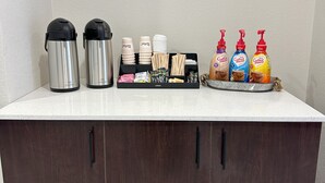A kitchen counter with two stainless steel coffee makers, a coffee mug, disposable cups, a tray with coffee sachets, and a bottle of hand sanitizer. - Red Roof Inn Cambridge, OH (Cambridge)