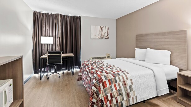 A hotel room with a bed, desk, chair, and a large window with curtains. - Red Roof Inn Cambridge, OH (Cambridge)