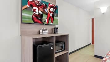 Habitación de hotel con una televisión de pantalla plana montada en la pared, un refrigerador negro, un microondas y una pequeña repisa con una cafetera y una caja de pañuelos.