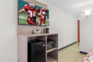 A hotel room with a flat-screen TV mounted on the wall, a black refrigerator, a microwave, and a small shelf with a coffee maker and a tissue box. - Red Roof Inn Cambridge, OH (Cambridge)