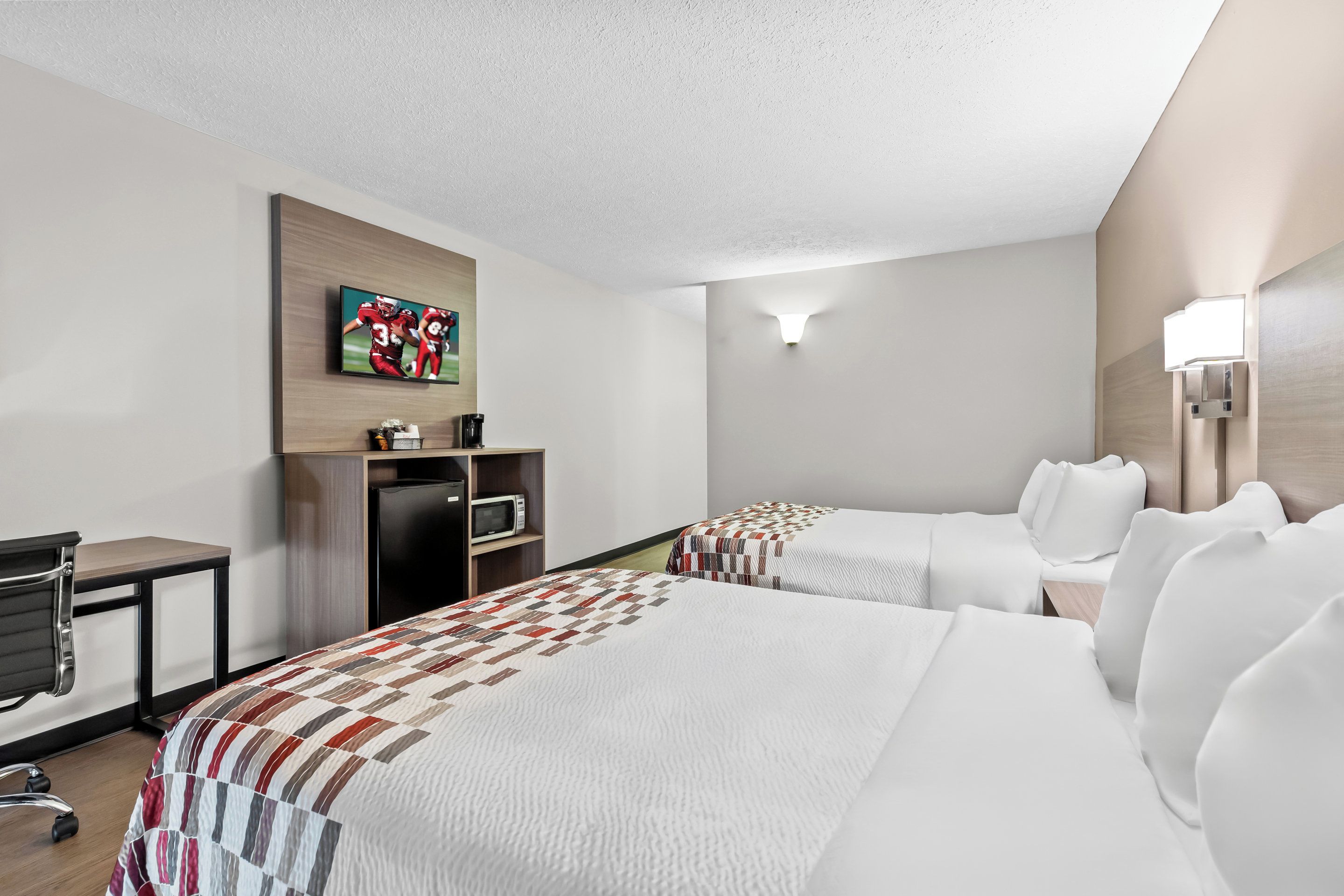 A hotel room with a large bed, a desk, a television, and a microwave.