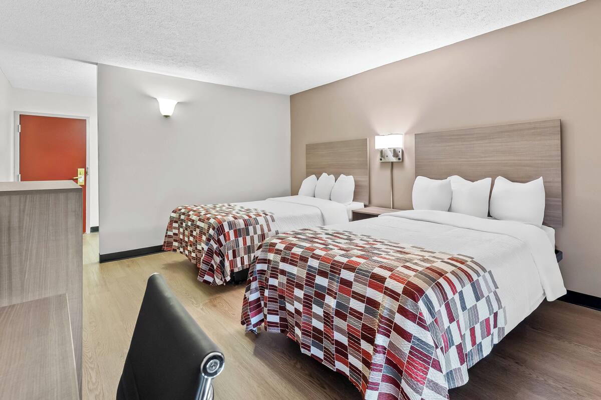 Quarto de hotel com duas camas, uma escrivaninha e uma cadeira.