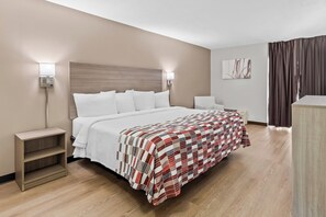 A hotel room with a bed, bedside tables, a nightstand, a chair, a desk, and a wall-mounted artwork. - Red Roof Inn Cambridge, OH (Cambridge)