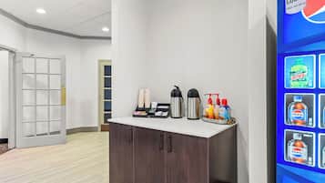 Uma área de recepção de hotel com balcão, estação de café e dispensador de bebidas.