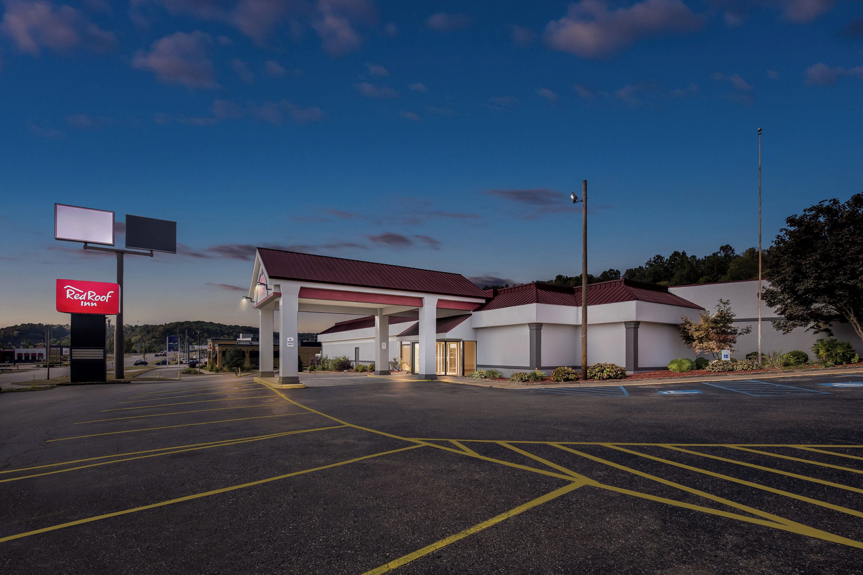 Un hôtel Red Roof Inn avec une station-service attenante, offrant une vue sur un ciel dégagé et un parking avec des places délimitées.
