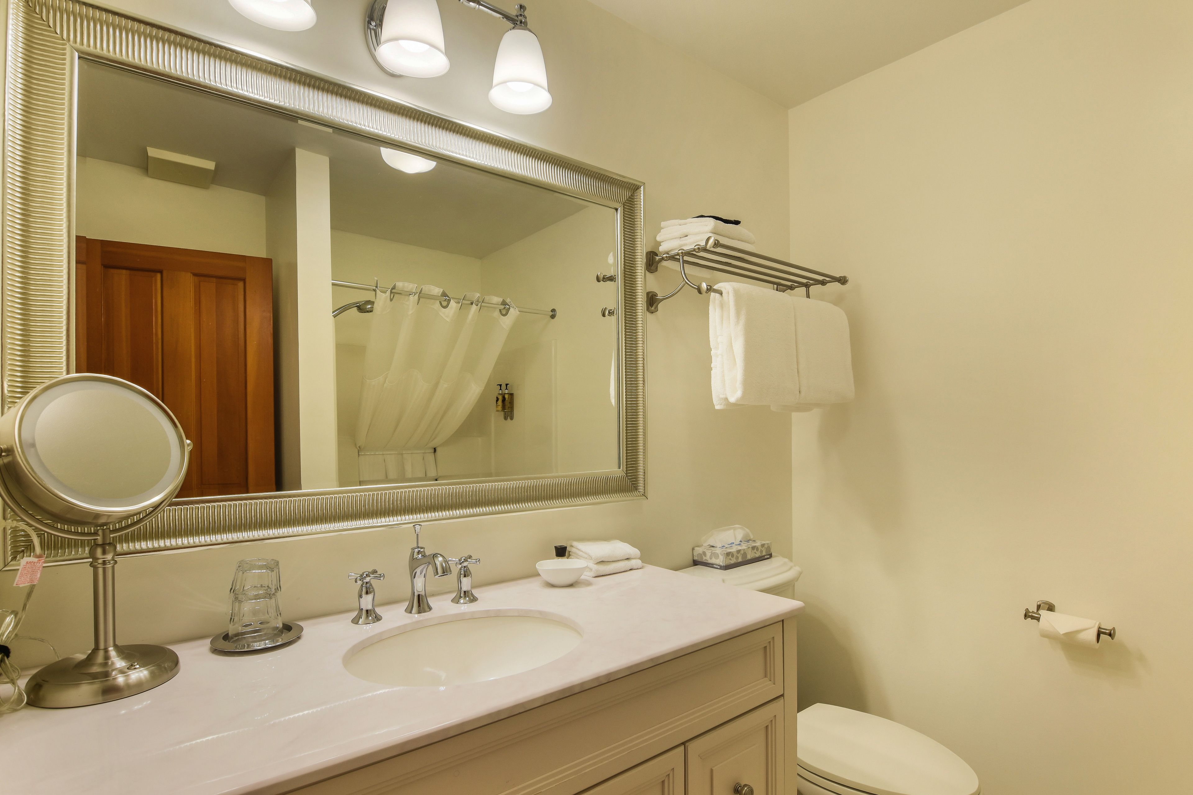 A bathroom with a large mirror, a sink, a toilet, and a towel rack.
