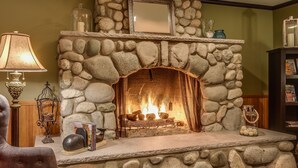 A cozy living room with a stone fireplace, a plush armchair, a lamp, and a bookshelf. - The Wild Iris Inn (La Conner)
