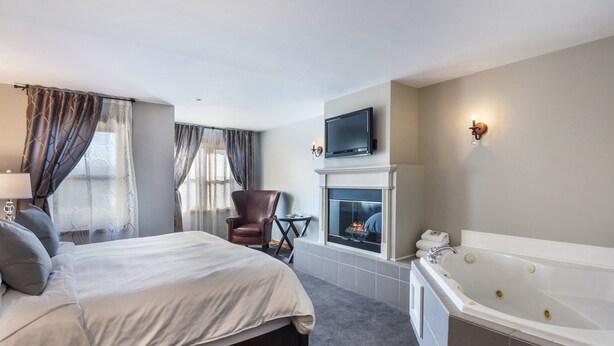 A hotel room with a large bed, a fireplace, a TV mounted above it, and a separate bathtub. - The Wild Iris Inn (La Conner)