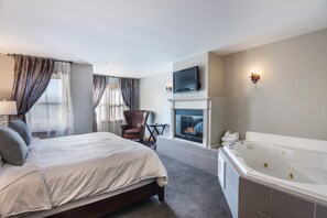 Habitación de hotel con una cama grande, una chimenea, un televisor montado arriba y una bañera independiente.