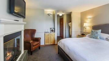 Une chambre d’hôtel avec une cheminée, un lit, un fauteuil en cuir marron, une table de chevet et un téléviseur fixé au mur.