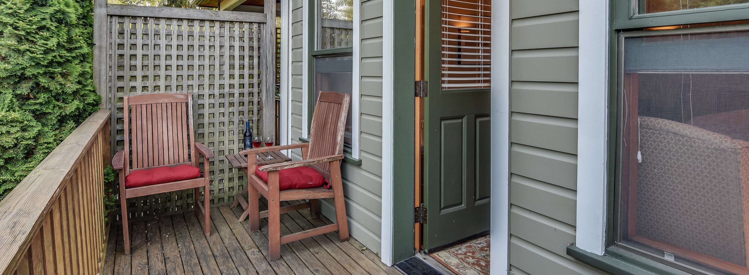 A wooden deck with two wooden chairs and a table, a wooden fence, and a door with a screen.