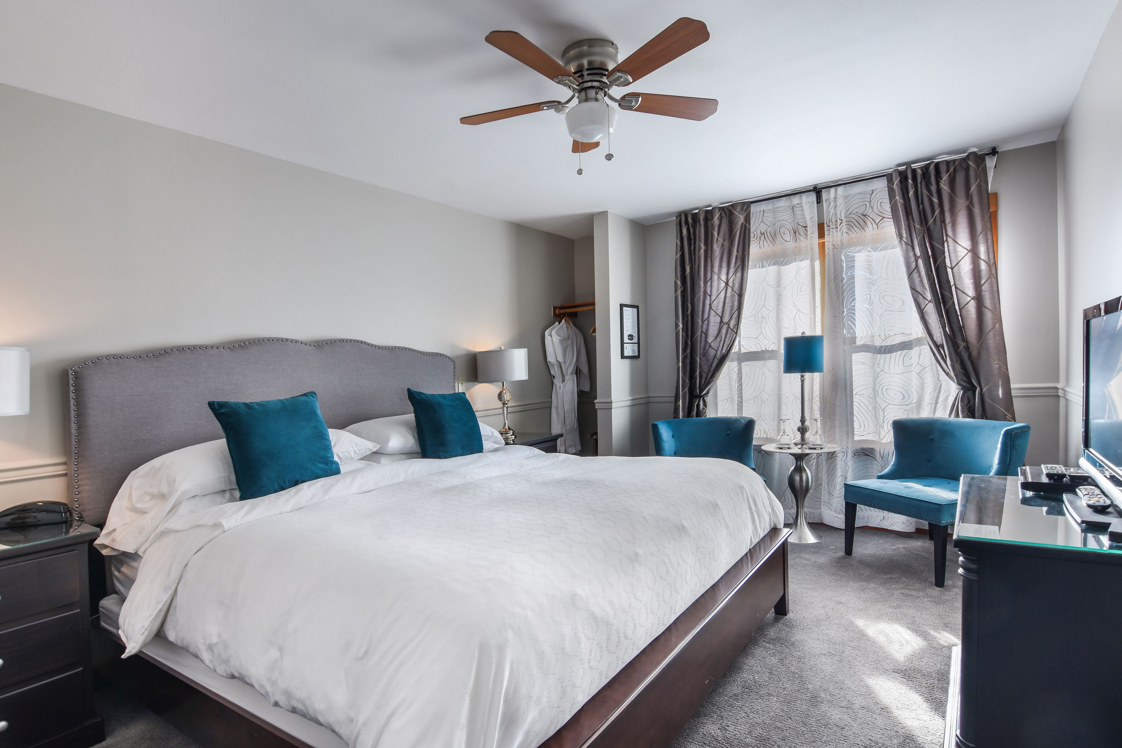 A hotel room with a large bed, a desk with a chair, a ceiling fan, and a TV.