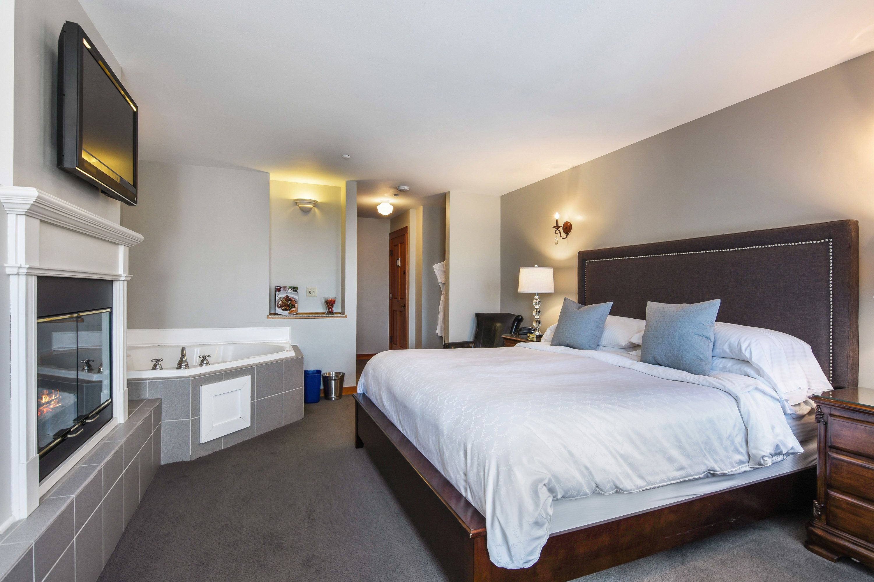 A hotel room with a large bed, a built-in fireplace, a bathtub, and a television mounted on the wall.