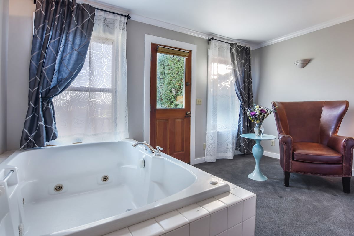 A bathroom with a large bathtub, a wooden door, and a brown leather chair.