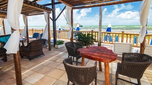 Un patio al aire libre con mobiliario de mimbre, una mesa de madera y vistas al océano.
