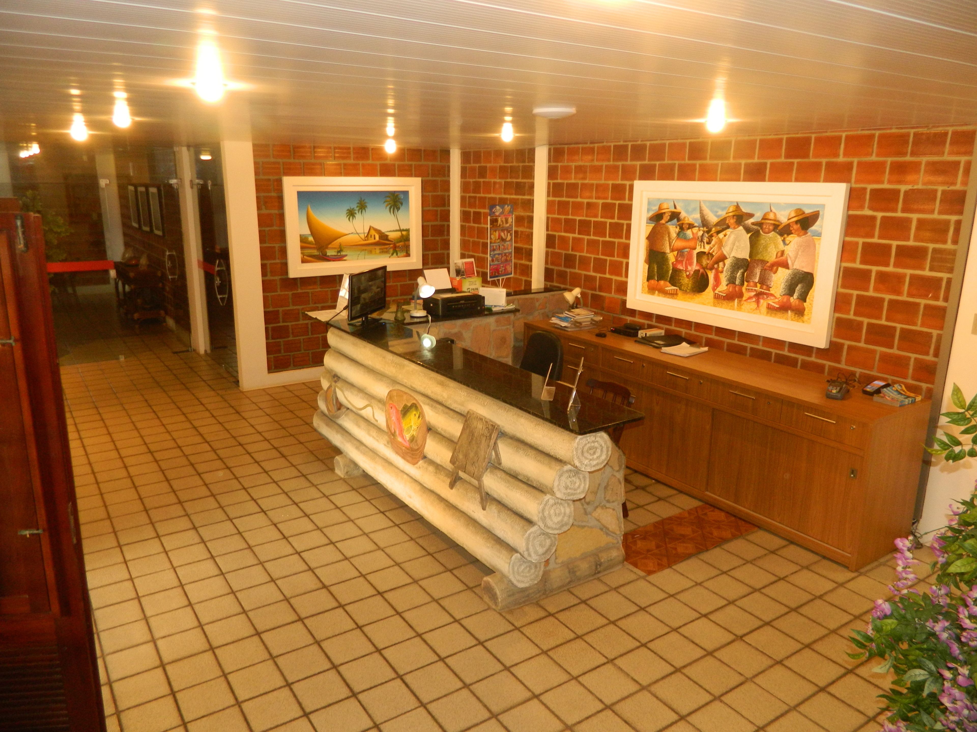 Una zona de recepción con pared de ladrillo, suelo de baldosas, escritorio de madera y cuadros enmarcados.