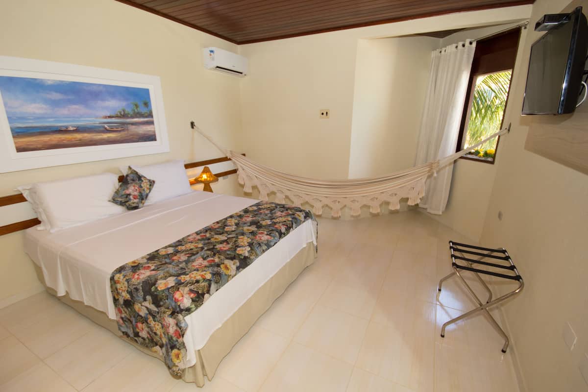 Um quarto com cama, rede, televisão e janela com cortinas.