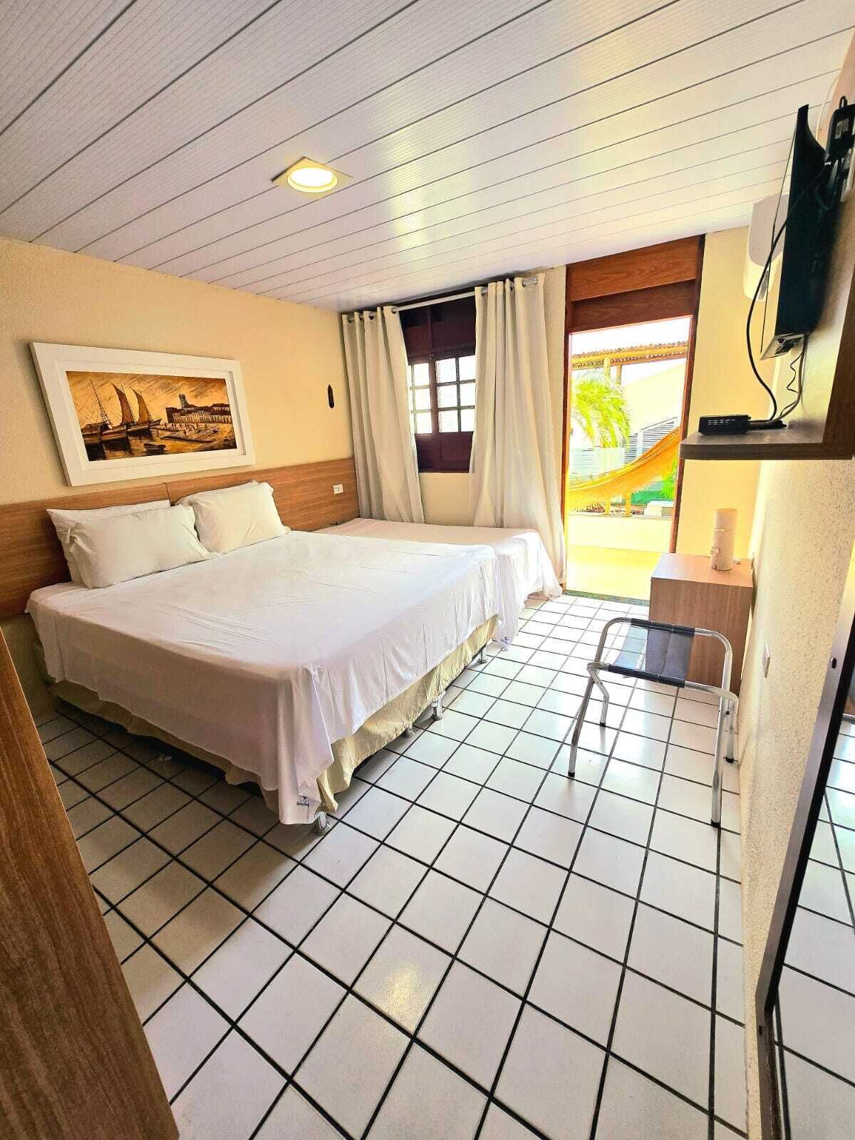Une chambre d’hôtel avec un lit, une chaise, une télévision et une fenêtre avec des rideaux.