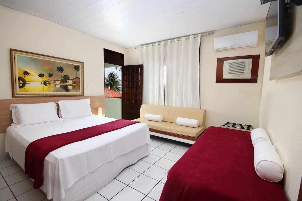 Quarto de hotel com cama, sofá, televisão e um quadro na parede.