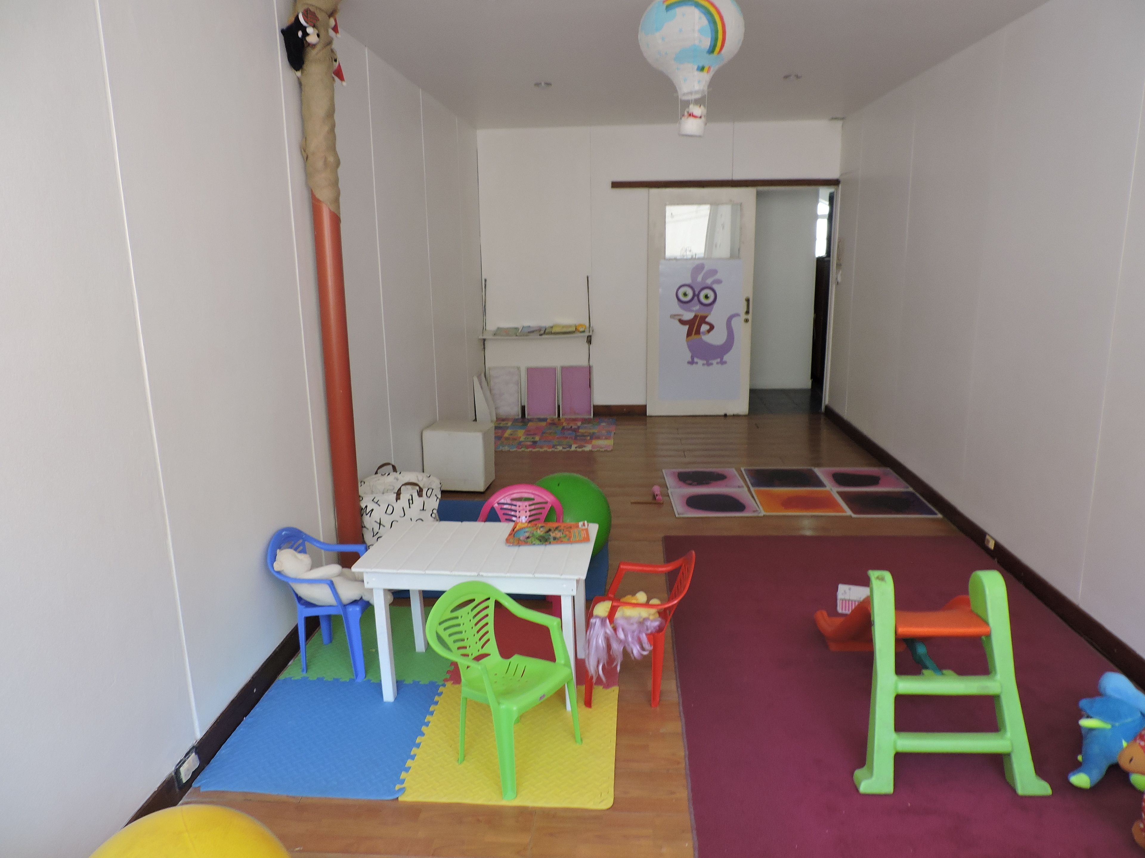 A children's playroom with colorful furniture and toys, a white table, and a play mat with a rainbow design.