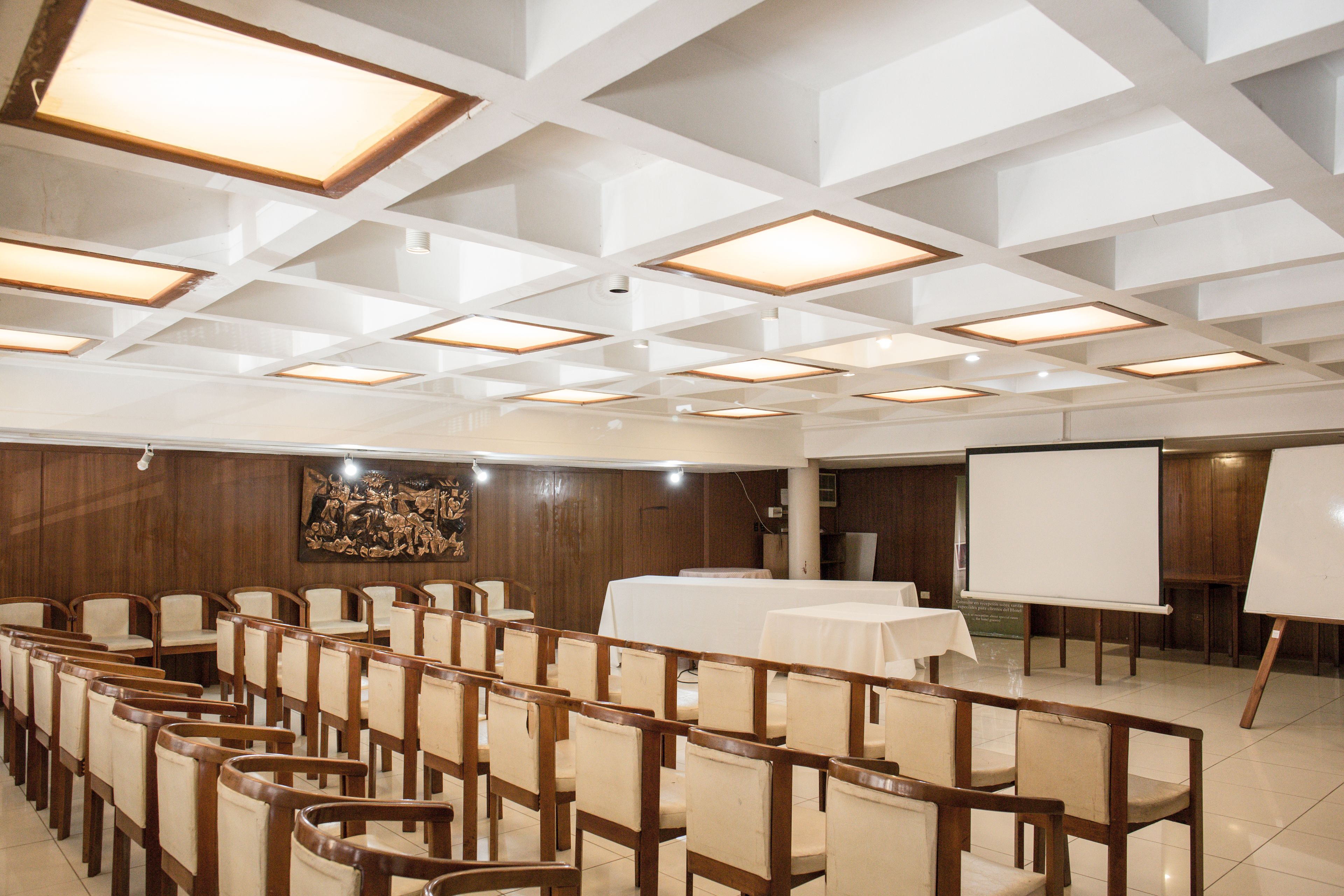 Une salle de conférence avec des rangées de chaises en bois, un tableau blanc et des tables.