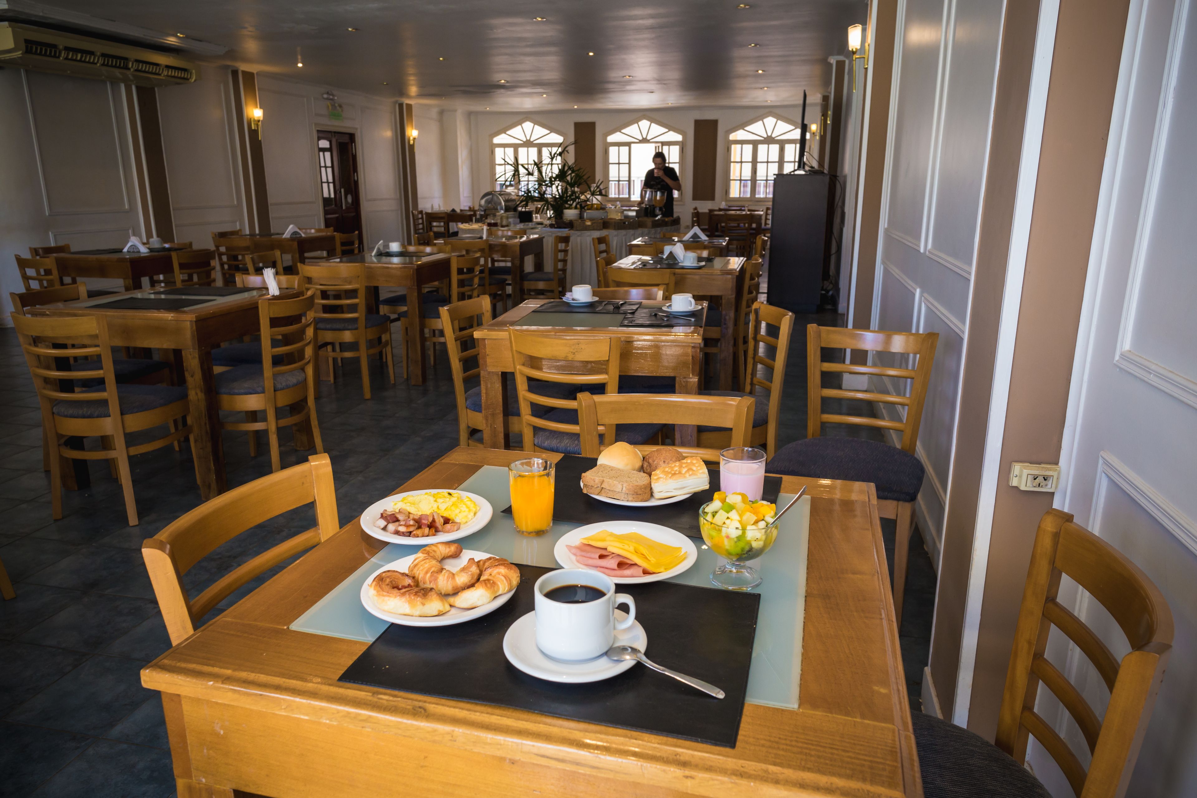 A dining area with multiple tables and chairs, breakfast plates with croissants, coffee, and juice.