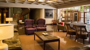 A lobby with a modern design, featuring a staircase, seating area with armchairs, a coffee table, and a TV mounted on the wall. - Julio Cesar Hotel (Posadas)