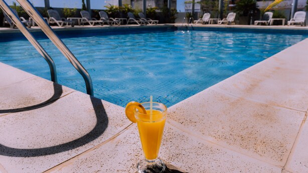 A swimming pool with lounge chairs and a glass of orange juice on the edge. - Julio Cesar Hotel (Posadas)