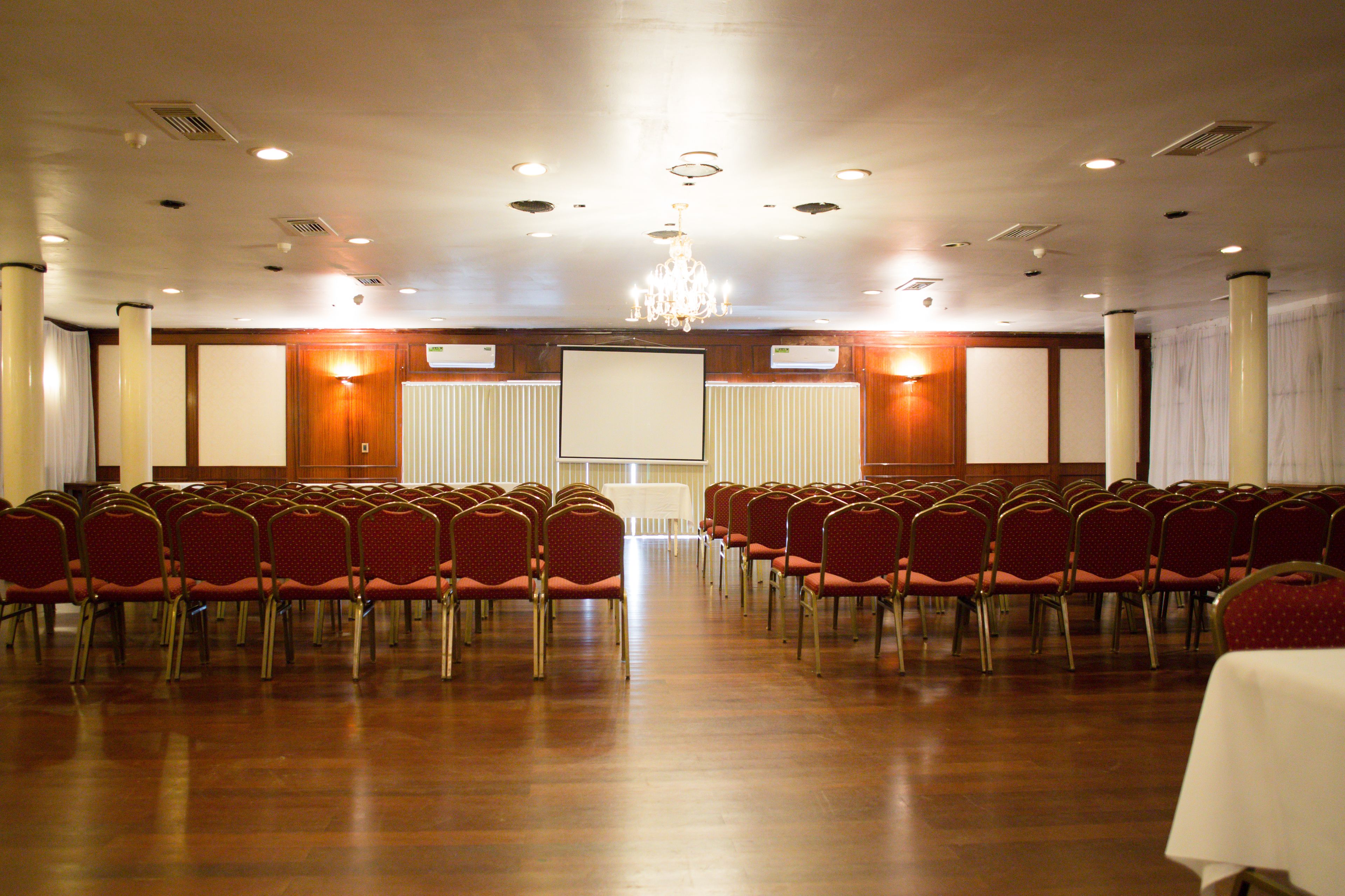 A conference room with rows of red chairs, a large screen, and a chandelier.