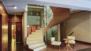 A modern hotel lobby with a curved staircase, a seating area with two chairs and a small table, and a potted plant. - Julio Cesar Hotel (Posadas)