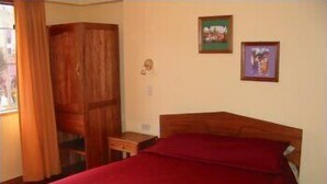 Quarto com cama de madeira, colcha vermelha, guarda-roupa de madeira e duas molduras na parede.