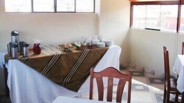 Uma área de jantar com uma mesa posta para dois, uma cadeira e uma janela com persianas.