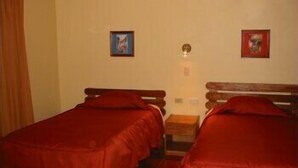 Quarto com duas camas de solteiro, uma mesinha e duas imagens emolduradas na parede.