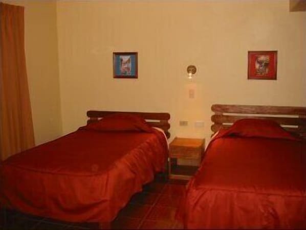 Une chambre avec deux lits simples, une petite table et deux tableaux encadrés au mur.