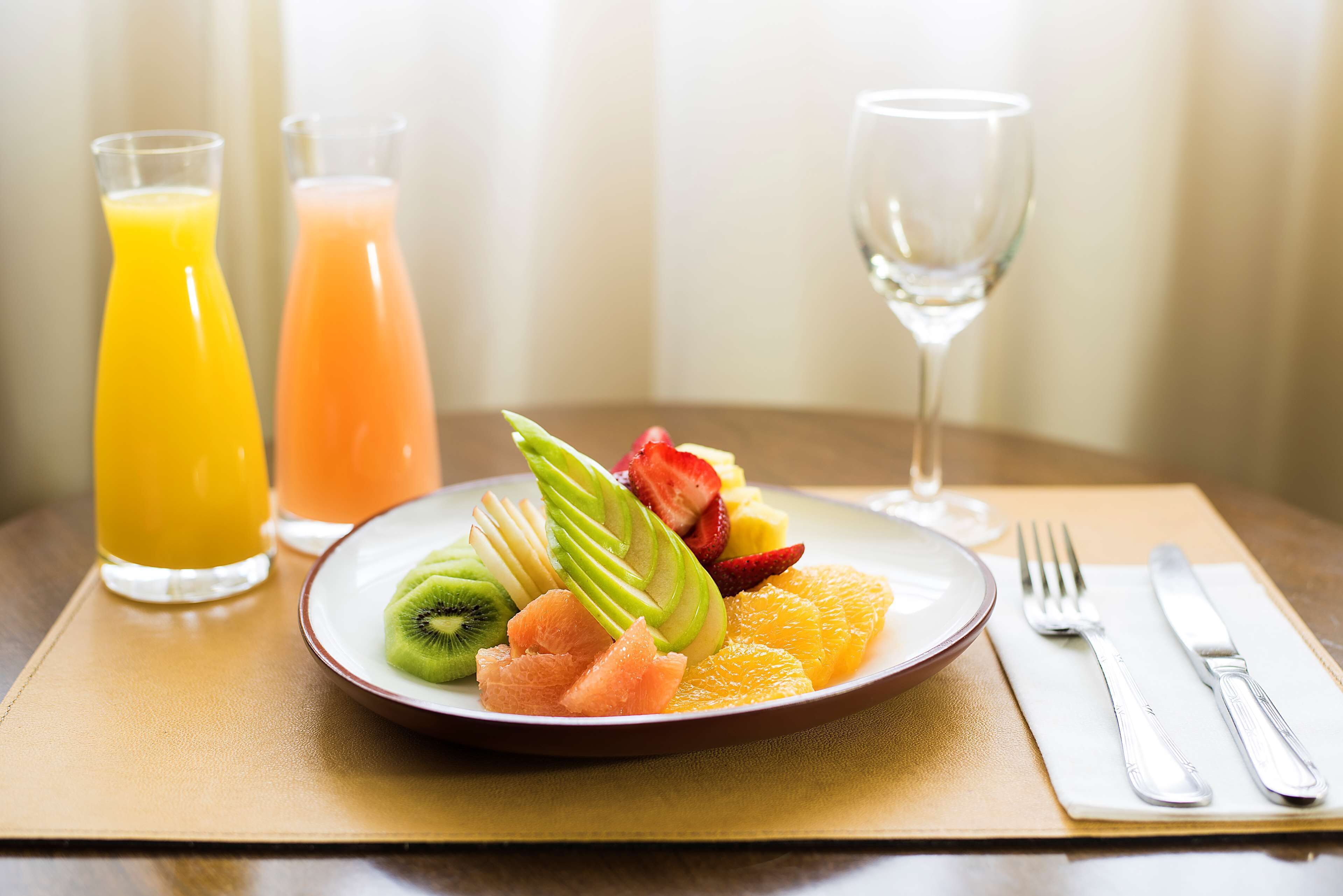 Disposição de mesa para o café da manhã, com uma travessa de frutas, dois copos de suco e uma taça de vinho.