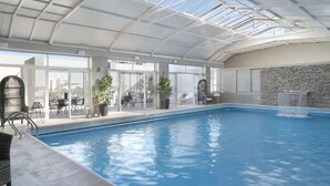 An indoor swimming pool with a glass ceiling, stone wall, and outdoor seating area. - NH Santiago del Estero (Santiago del Estero)