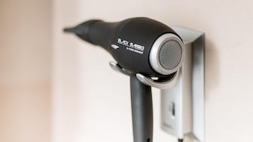 Secador de cabelo preto fixado na parede, ligado a uma tomada.