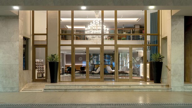 The entrance of NH Santiago del Estero hotel with a modern design, featuring a chandelier, seating area, and potted plants. - NH Santiago del Estero (Santiago del Estero)