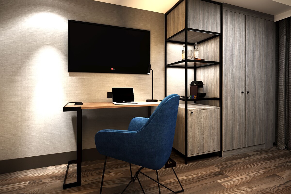A modern room with a wooden desk, a blue chair, a TV mounted on the wall, and a built-in wardrobe with shelves.