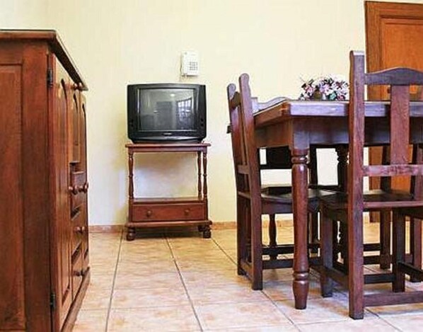 A wooden dining table with chairs, a television on a stand, and a cabinet.