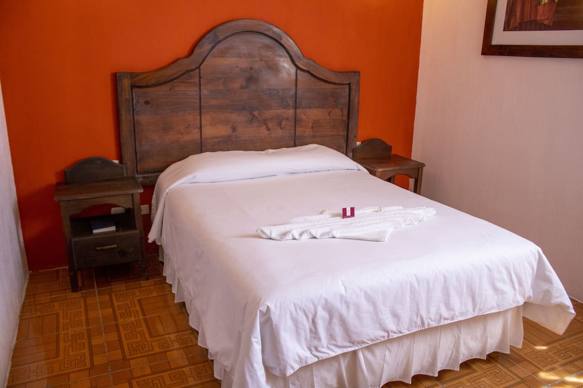 Una cama bien hecha con sábanas blancas, un cabecero de madera y una mesita de noche con una lámpara.
