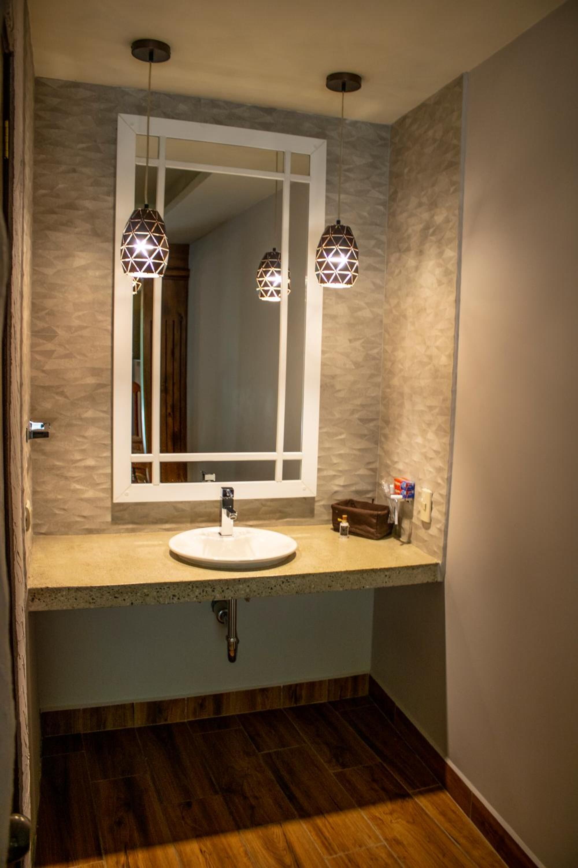 A bathroom with a white sink, two geometric pendant lights, a mirror, and a wooden floor.